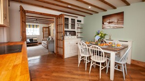 Un'ampia cucina con travi in legno, un'area pranzo con sedie bianche e vista sul soggiorno.