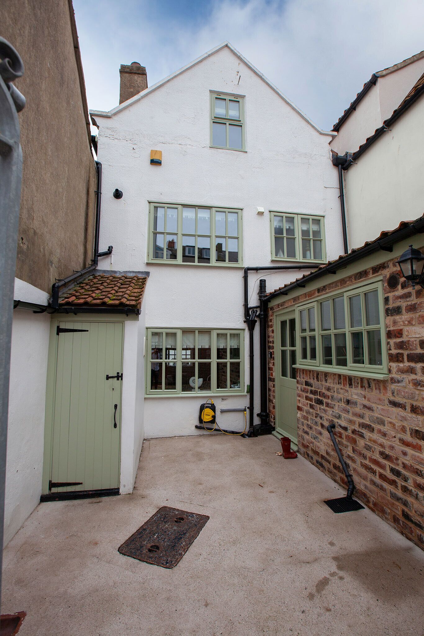 A narrow alleyway with a white building featuring green-framed windows and a tiled roof.