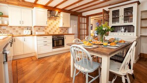 Una cucina con travi in legno, mobili bianchi, un tavolo da pranzo apparecchiato per la colazione e vista sull'area pranzo.
