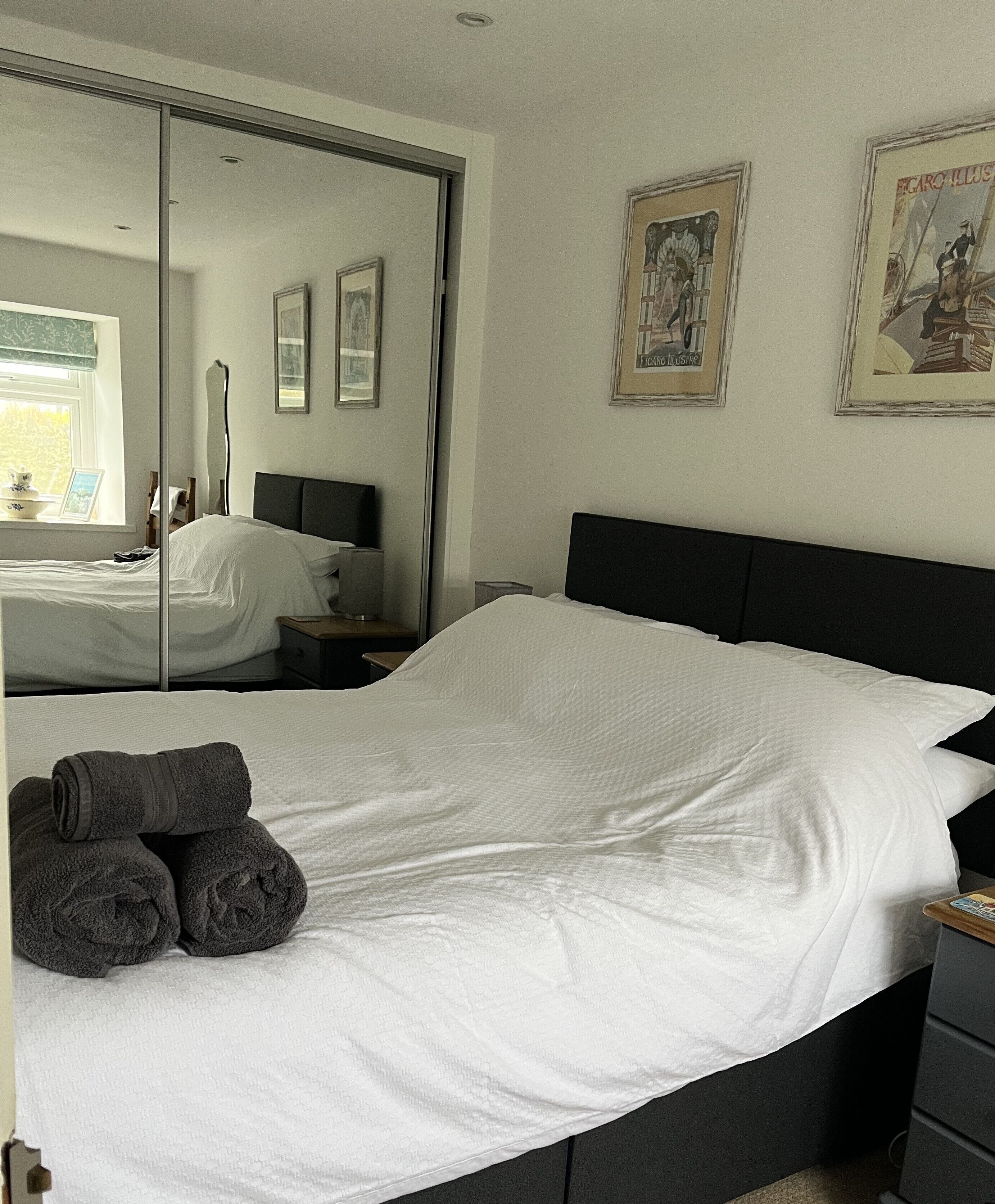 A hotel room with a large bed, a bedside table, a mirror, and artwork on the wall.