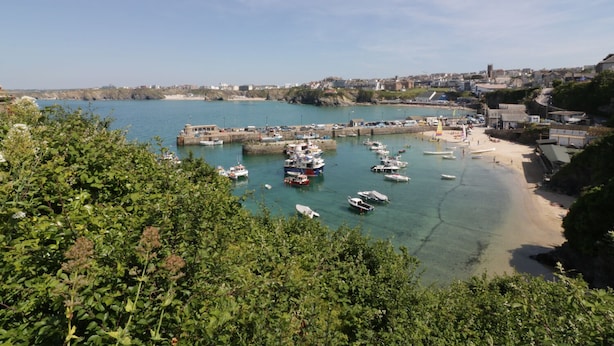 Uma cidade costeira com um porto cheio de barcos, uma praia arenosa e uma mistura de edifícios residenciais e comerciais.