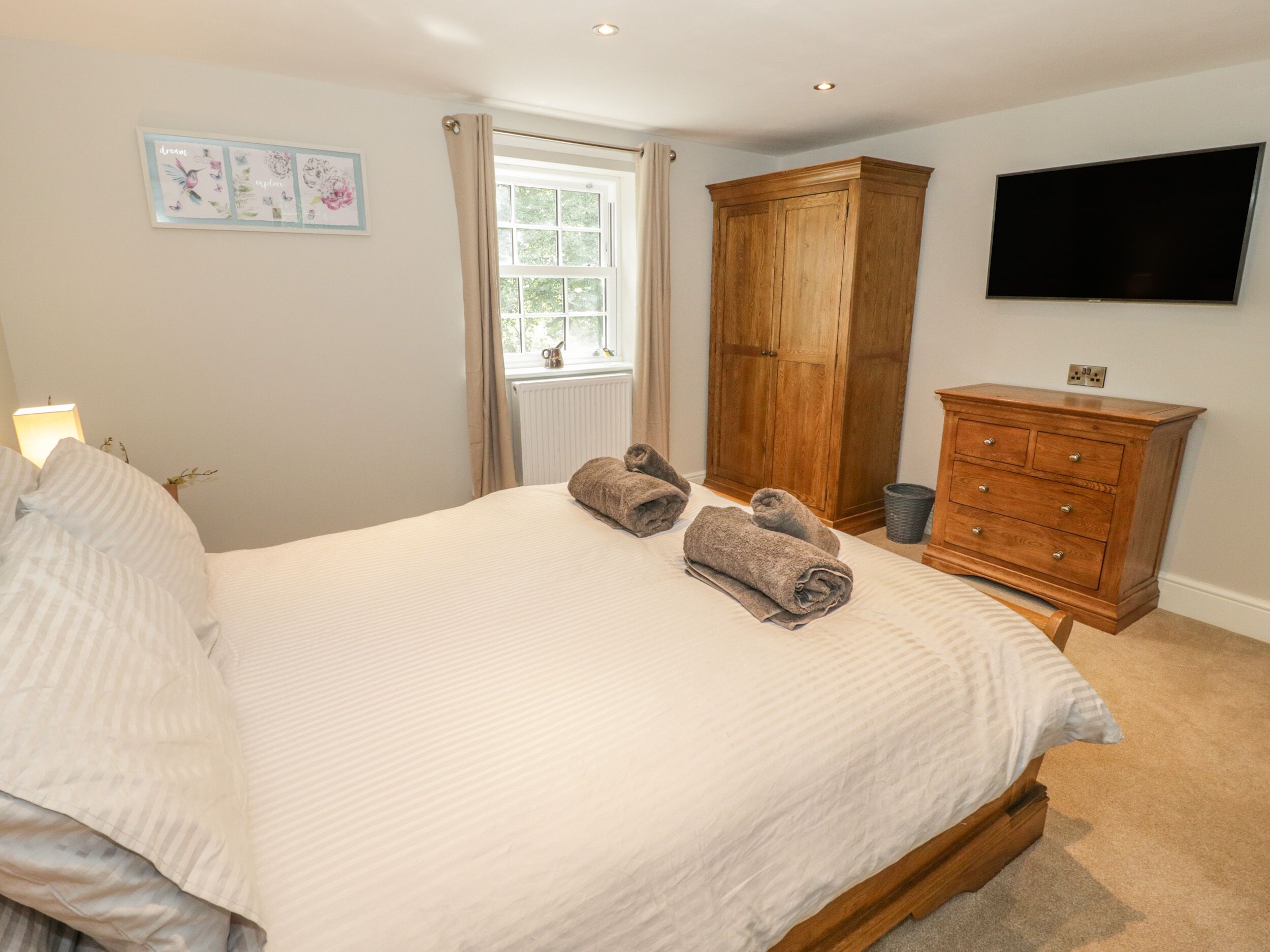 A bedroom with a large bed, a wooden wardrobe, a flat-screen TV, and a window with curtains.
