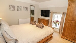 A bedroom with a large bed, a wooden wardrobe, a dresser, a mirror, and a TV on the wall. - Bryn Derwen Coach House (Bangor)