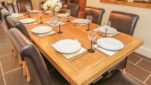A dining area with a long wooden table set for six, surrounded by leather chairs. - Bryn Derwen Coach House (Bangor)