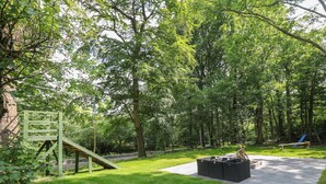 A grassy outdoor area with a wooden play structure and a concrete seating area. - Bryn Derwen Coach House (Bangor)