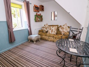 Een gezellige kamer met een kamerbreed tapijt, een bank met gestreepte kussens, een klein krukje, een metalen tafeltje en een raam met gordijnen.