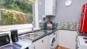 A compact kitchen with a washing machine, a microwave, and a red refrigerator. - River Cottage (Port Talbot)