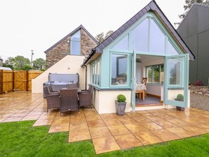 Una casa con un patio que cuenta con una barbacoa, mobiliario de mimbre y un pequeño jardín.