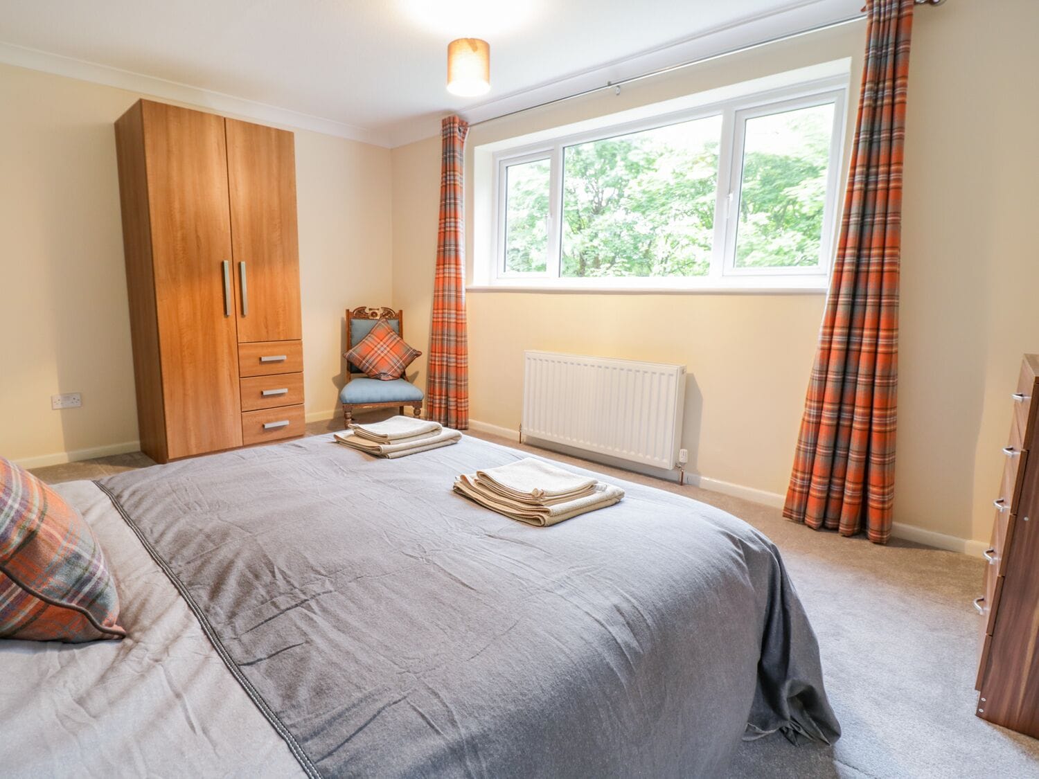 A bedroom with a bed, a wardrobe, a chair, a radiator, and a window with curtains.