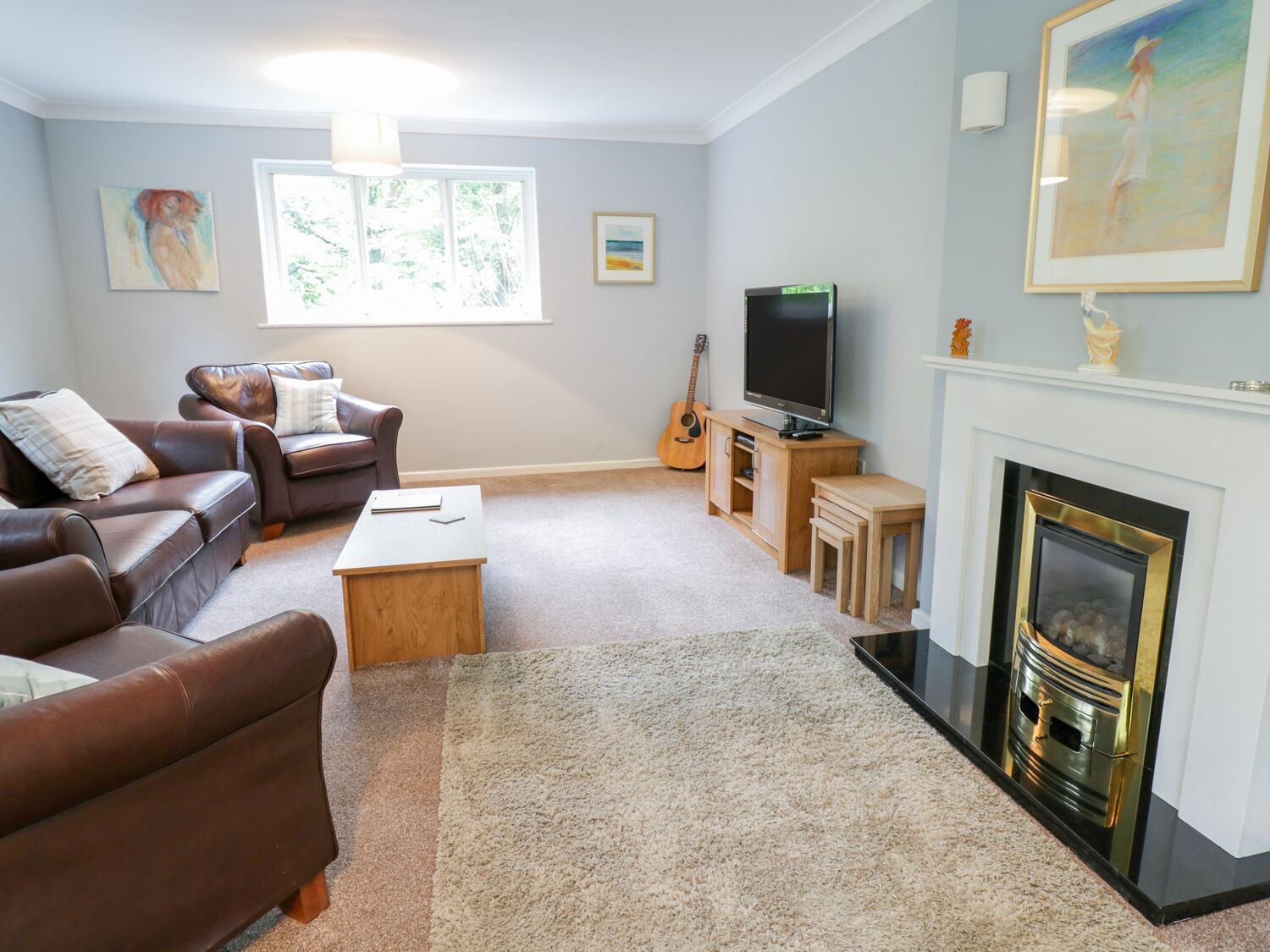 A living room with a fireplace, leather sofas, a TV, and artwork on the walls.
