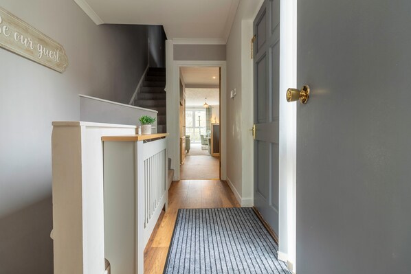 A hallway with a staircase, a door with a brass handle, and a doormat. - Fishertown House (Nairn)