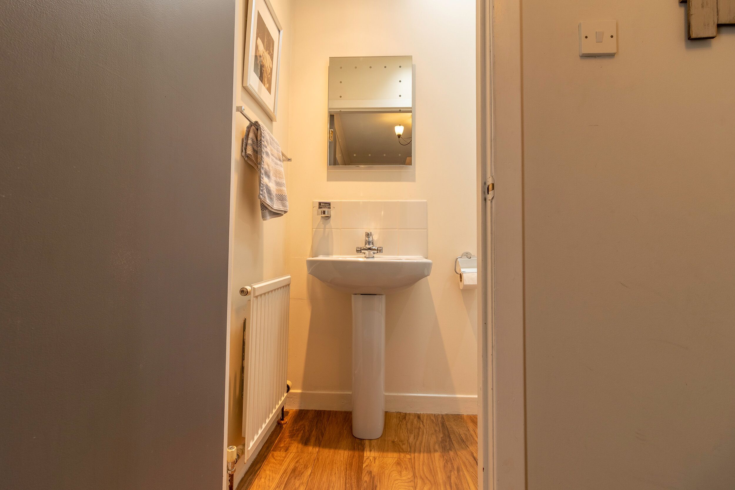 A small bathroom with a white pedestal sink, a mirror above it, and a towel hanging on the wall.