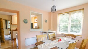 A dining area with a table set for four, wooden chairs, a white radiator, a mirror, and a window with blinds. - Dyfi Cottage (Machynlleth)