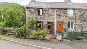 A stone house with a wooden door, a small window, and a visible chimney. - Dyfi Cottage (Machynlleth)