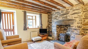 A cozy living room with a stone fireplace, wooden beams, and comfortable seating. - Dyfi Cottage (Machynlleth)