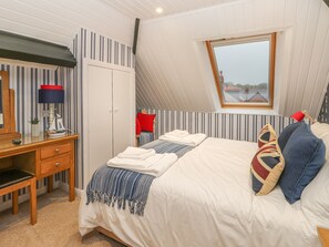 A bedroom with a sloped ceiling, a large bed with multiple pillows, a bedside table with a lamp, a wardrobe, and a window with a view of buildings. - Hillcrest (Scarborough)