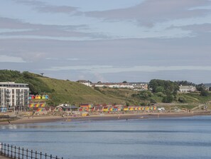 A coastal area with a beach, colorful beach huts, and residential buildings on a hillside. - Hillcrest (Scarborough)