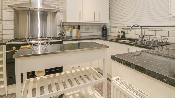 A modern kitchen with white cabinets, a stainless steel range hood, a black countertop, and a built-in sink. - Hillcrest (Scarborough)