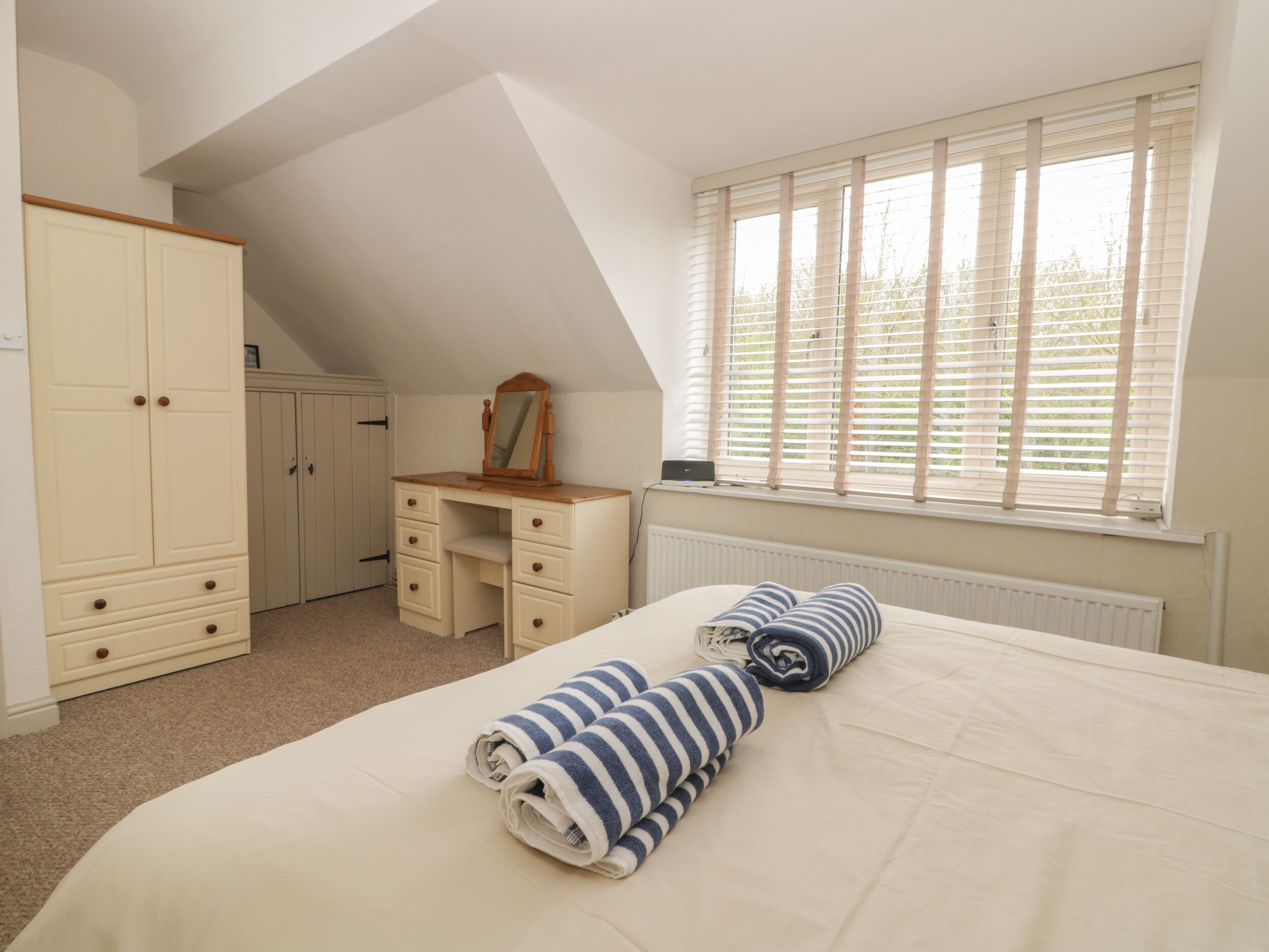 A bedroom with a bed, a dresser, a mirror, and a window with blinds.