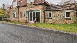 A stone house with a tiled roof, a glass door entrance, and a small attached shed. - Wyke Lodge Cottage (Scarborough)