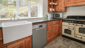 A kitchen with wooden cabinets, a dishwasher, a microwave, and a stove. - Wyke Lodge Cottage (Scarborough)