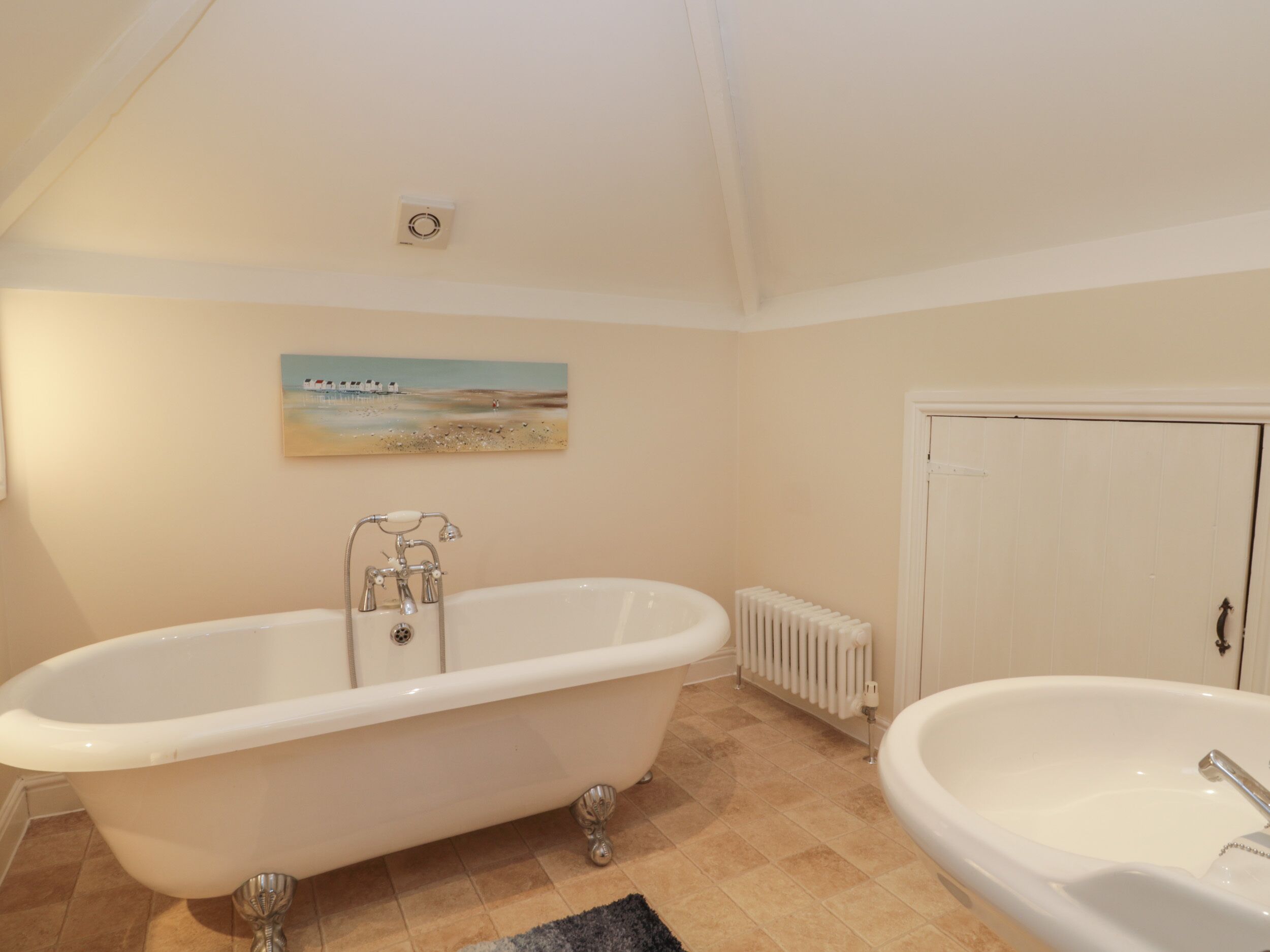 A bathroom with a freestanding bathtub, a sink, a radiator, and a door.
