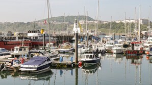 A marina with various boats docked, a lighthouse in the background, and a hilly landscape with buildings. - Wyke Lodge Cottage (Scarborough)