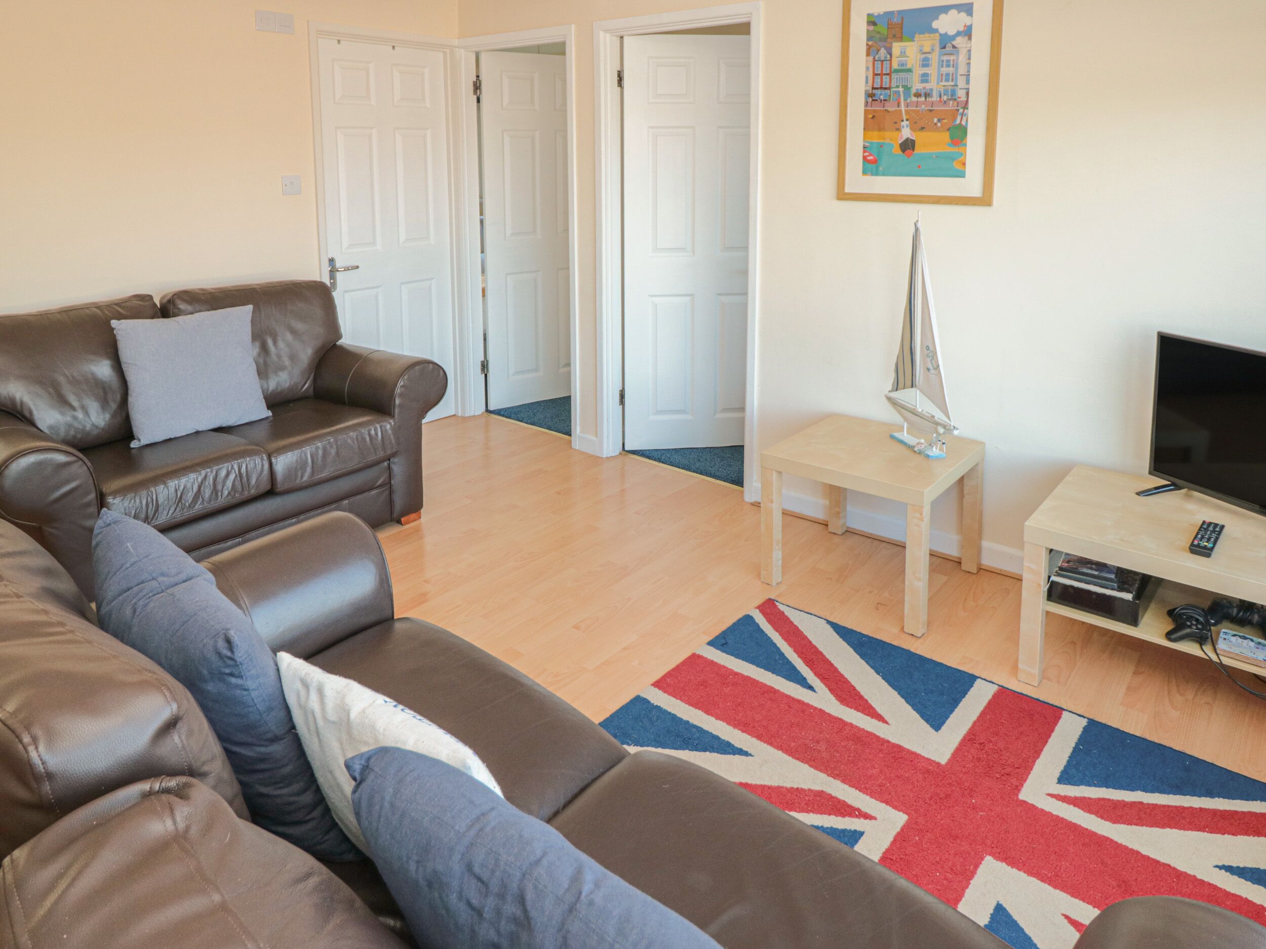 A living room with a brown leather sofa, a small wooden table, a television, and a Union Jack rug.