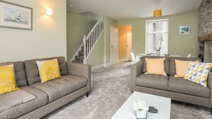 A living room with two grey sofas, a white coffee table, and a staircase leading to another room. - Maes-yr-haf (Criccieth)