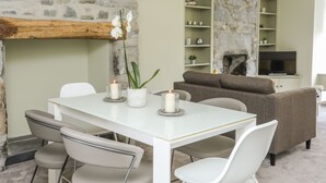 A modern living room with a stone fireplace, a dining table with chairs, and a sofa. - Maes-yr-haf (Criccieth)