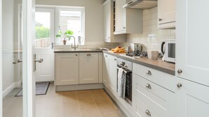 A modern kitchen with white cabinets, a built-in oven, and a microwave. - Maes-yr-haf (Criccieth)