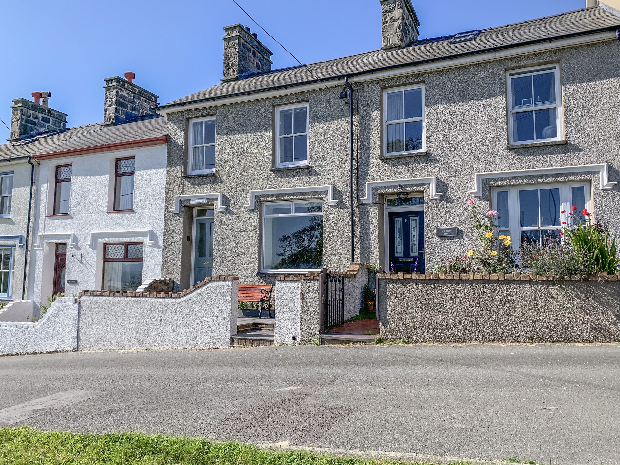 A row of stone houses with multiple windows, a front entrance, and a small garden with flowers.