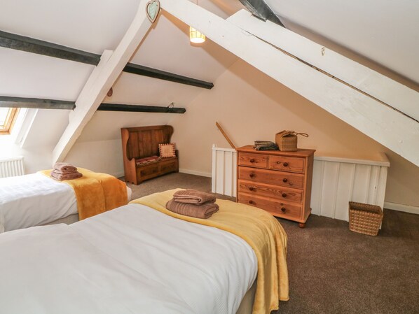 Ein gemütliches Schlafzimmer im Dachgeschoss mit zwei Betten, einer Holzkommode und einer Bank.