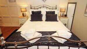 A neatly made bed with two pillows, two bedside tables with lamps, a wall-mounted decorative item, and a door. - Gavel Cottage (Whitby)