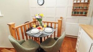 A dining area with a round table, two chairs, a clock, and a shelf with mugs. - Gavel Cottage (Whitby)