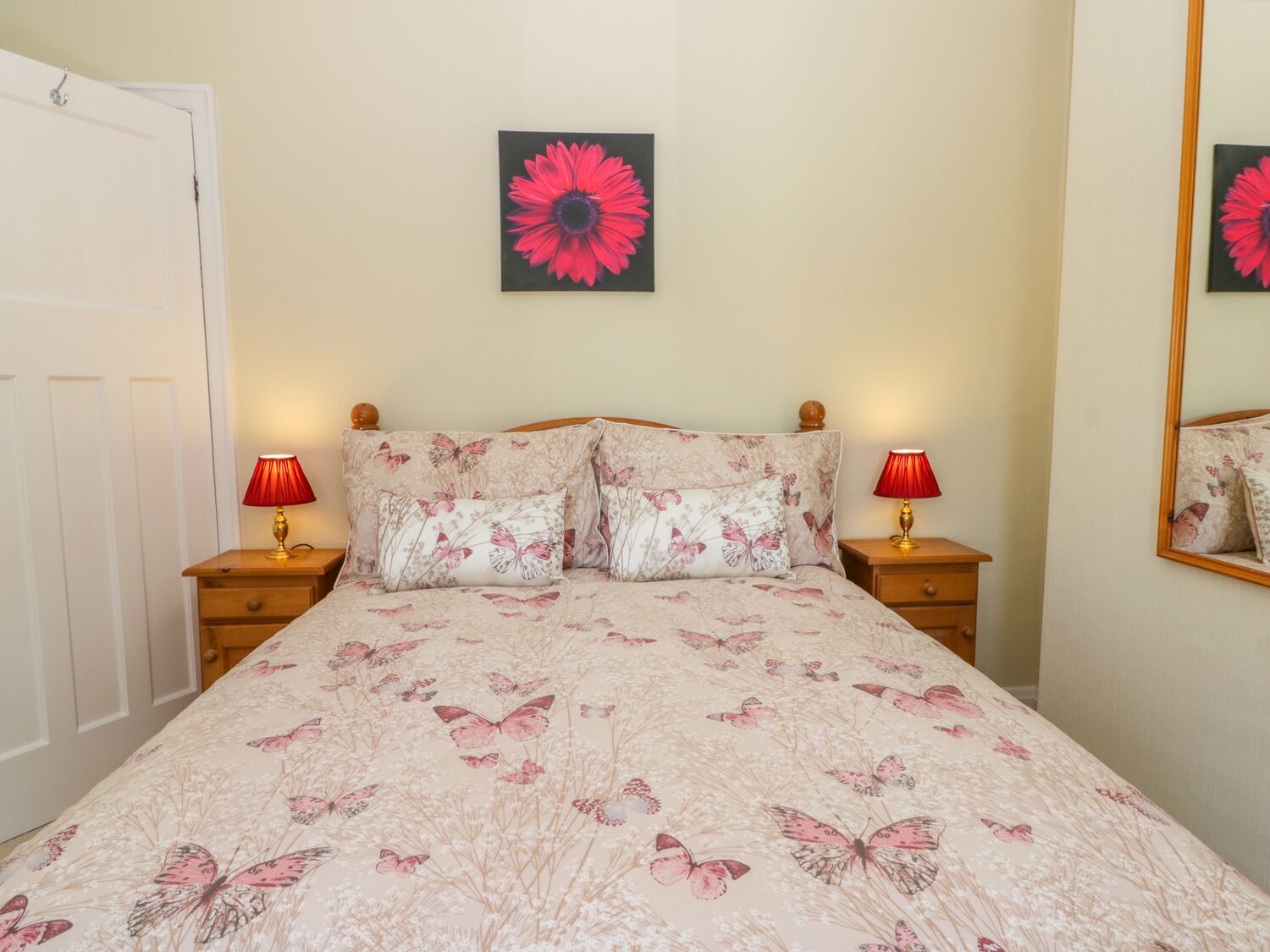Une chambre à coucher avec une couvre-lit à motifs floraux, deux lampes de chevet, un grand miroir et une porte.
