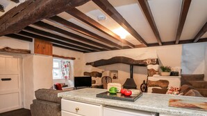 Une cuisine dotée d’un plan de travail en marbre, de poutres en bois, d’un mur en pierre et d’un coin salon accueillant avec un fauteuil rouge.