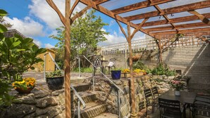 Un espace extérieur abrité, doté d’un escalier en pierre, d’une pergola en bois, de plantes en pot et de mobilier d’extérieur.