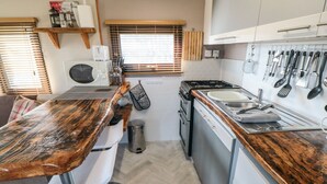 A compact kitchen with a wooden countertop, a sink, and a stove. There are utensils hanging on the wall and a trash can. - Castle View Cabin (Scarborough)