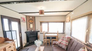 A cozy living room with a fireplace, wooden furniture, and a sofa with plaid cushions. - Castle View Cabin (Scarborough)