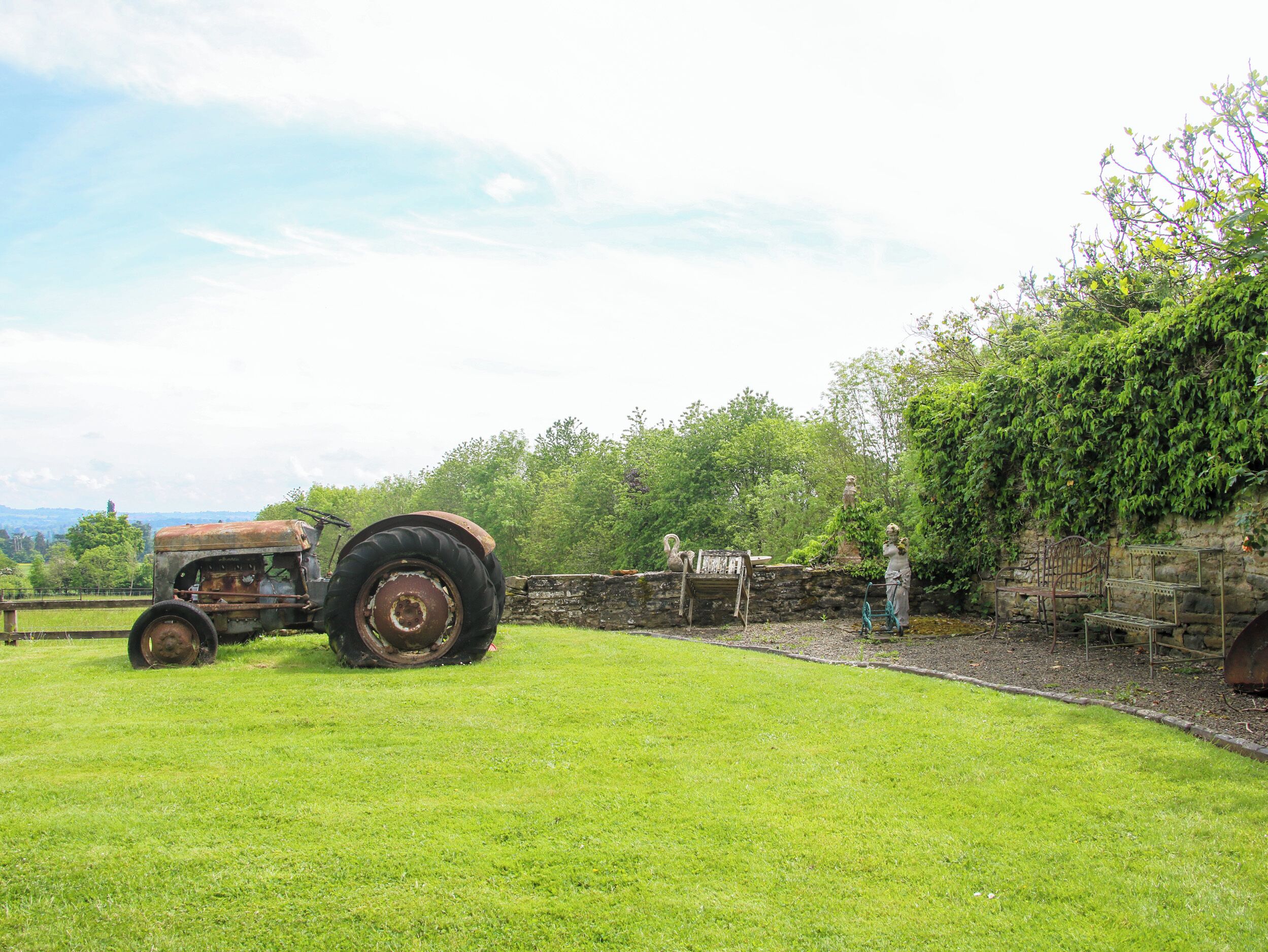A grassy field with a vintage tractor and a stone wall with a statue.