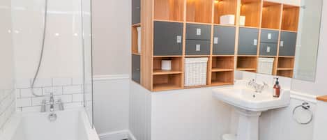 A modern bathroom with a bathtub, a sink, and a mirror. There are wooden cabinets above the sink and a shower area to the left.