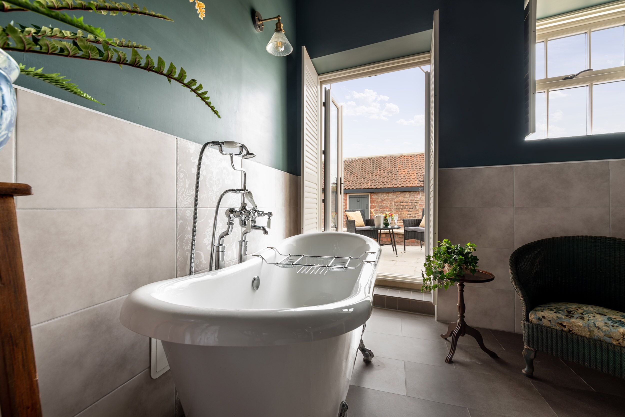 Une salle de bain avec une baignoire sur pieds, une douche et une petite table agrémentée d’une plante.