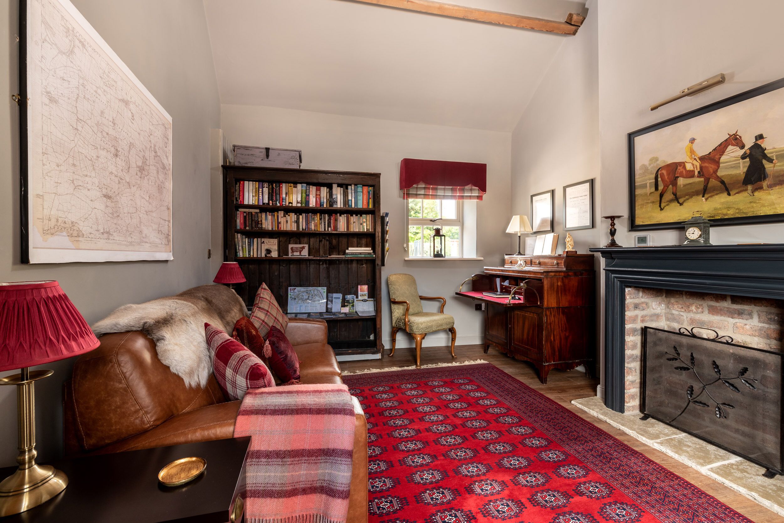A cozy living room with a leather sofa, a red patterned rug, a bookshelf, and a fireplace.