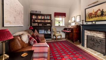 A cozy living room with a leather sofa, a red patterned rug, a bookshelf, and a fireplace.