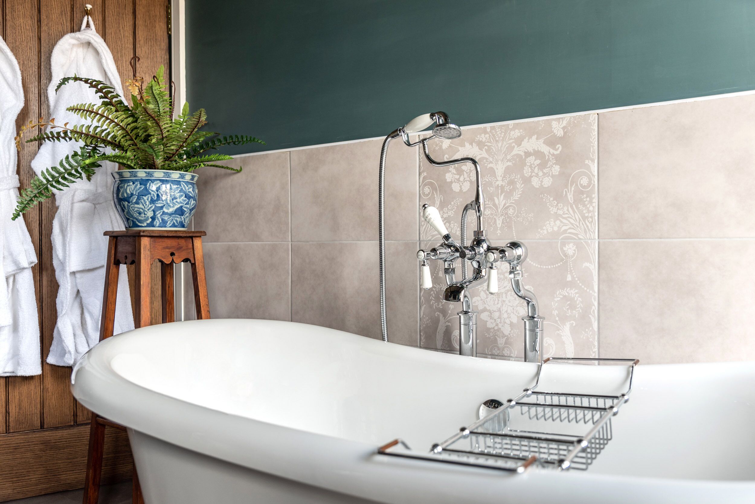 Ein Badezimmer mit freistehender Badewanne, Duschkopf, einer Zimmerpflanze und einem Handtuchhalter mit weißen Handtüchern.