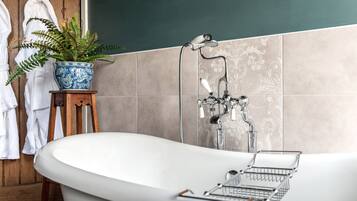 Ein Badezimmer mit freistehender Badewanne, Duschkopf, einer Zimmerpflanze und einem Handtuchhalter mit weißen Handtüchern.