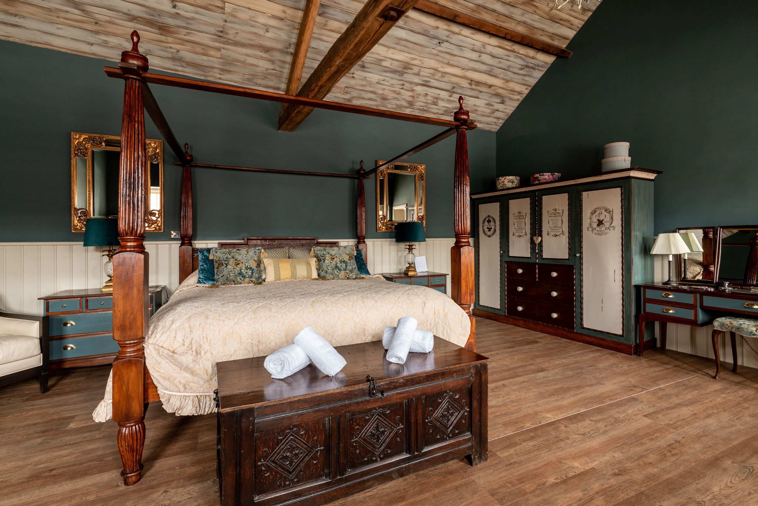 A four-poster bed with a wooden headboard, a wooden chest of drawers, and a dresser with multiple drawers and a mirror.