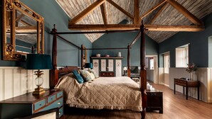 A four-poster bed with a quilted bedspread, a wooden ceiling with exposed beams, a large ornate mirror, and a dresser with drawers. - Sykes Lodge (Malton)