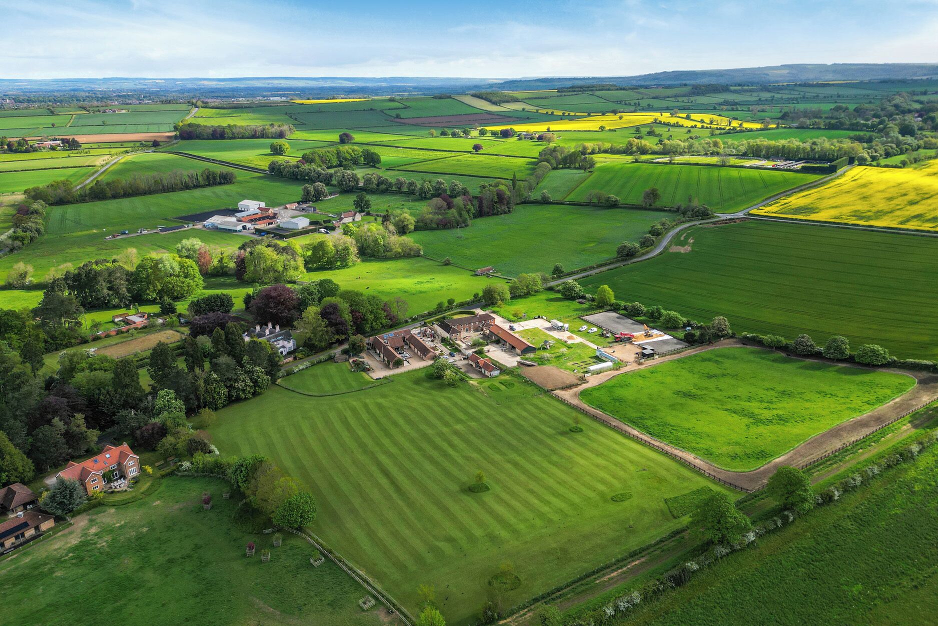 An aerial view of a rural landscape with fields, a farmhouse, and a small cluster of buildings.